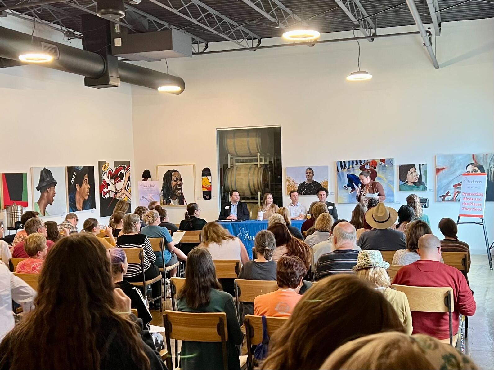 One-hundred Audubon members are seated at Upland FSQ Brewery in Indianapolis for Birds and Brews, facing a table of panelists with art on the wall behind them. Credit: Audubon Great Lakes 