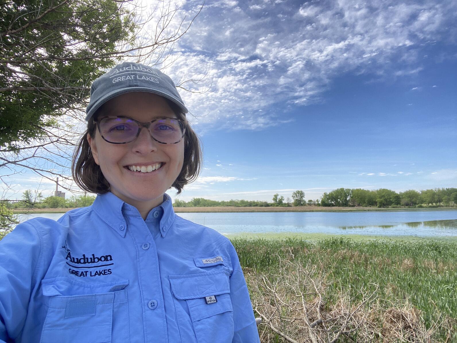 Stephanie Beilke, Senior Manager of Conservation Science with Audubon Great Lakes, snaps a selfie while in the field. A wetland and blue sky are in the background. 